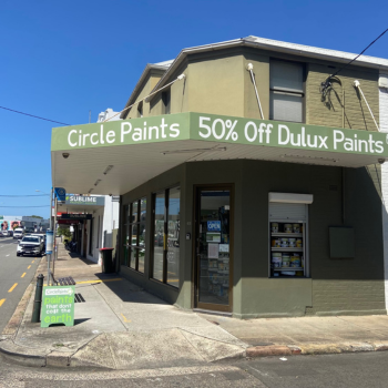 A corner storefront of Circle Paints with a green awning advertising 50% Off Dulux Paints. A sidewalk sign reads paints that don’t cost the earth.